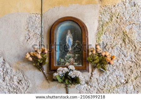 Typical Italian saint picture with plastic flowers decoration in the island capital Portoferraio on the island of Elba in Italy under a bright blue sky in summer