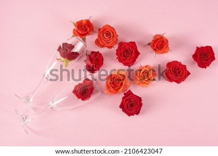 Red and orange roses are poured from glasses on a pink background. Aesthetics and beauty.                               Royalty-Free Stock Photo #2106423047
