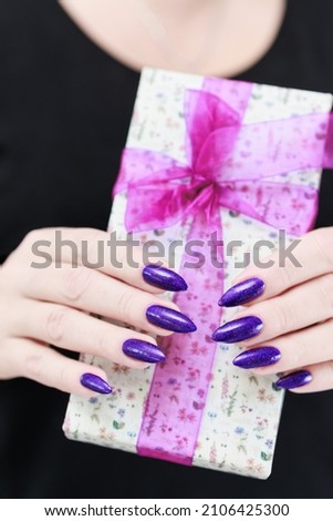 Female hands with long nails hold a gift box in purple colors