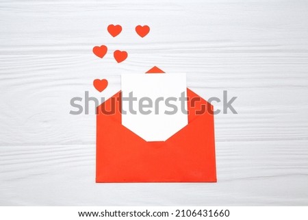 Red envelope with a white sheet of paper and red hearts on a white wooden background. Valentine's day greeting card.