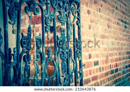 Old forging gate with ornament (entry to abandoned manor) and red stone brick wall. Selective focus on the remote side of the fence. Aged photo.