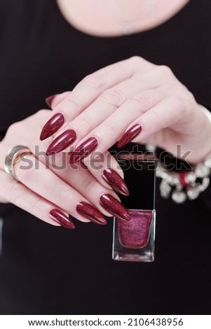 Female hands with long nails and dark red burgundy manicure holding a bottle of nail polish