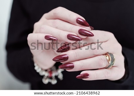 Female hands with long nails and dark red burgundy manicure holding a bottle of nail polish