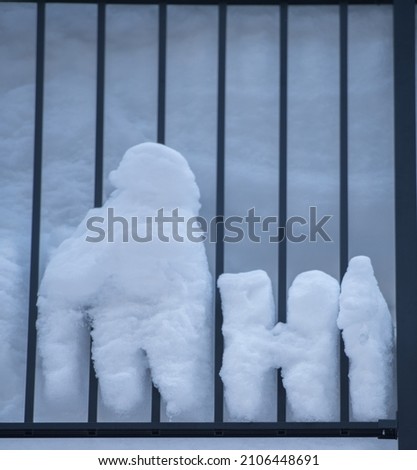 snow pushed through spaces of balcony railing  looking like small snow people behind bars vertical lines of fence bars white snow pushed through seaonal winter exterior 