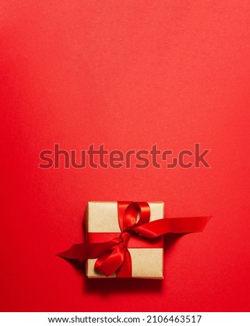Brown paper gift box with a red satin ribbon bow on top on red background. Christmas holiday mother and father Valentines days and birthday present flat lay concept with copy space
