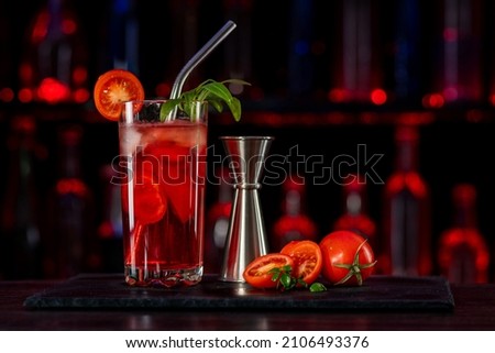 Cocktail Bloody Mary with ice on bar counter in a restaurant, pub. Red drink with virgin tomato juice. Fresh prepared alcoholic cooler beverage at nightclub. Showcases with bottles on dark background