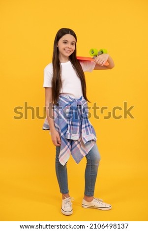 Happy teenage girl in teen casual holding pennyboard yellow background, skater girl