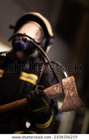 female firefighter portrait wearing full equipment, oxygen mask, and an axe. smoke and fire trucks in the background. 
