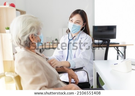 Asian doctor talk with old female patient about disease symptom, doctor use stethoscope listening lung of patient, elderly health check up , they wear surgical mask on white background, corona virus  Royalty-Free Stock Photo #2106551408