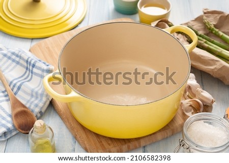 Yellow dutch oven on a wooden board with condiments around it Royalty-Free Stock Photo #2106582398