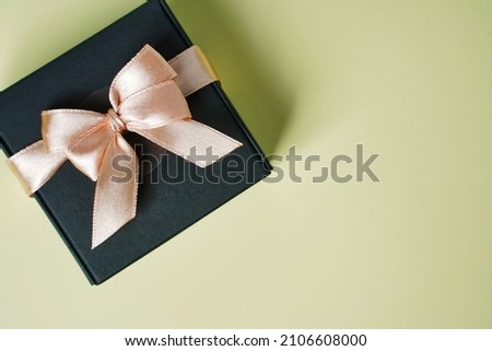 Dark gift present box with ribbon and bow on yellow background top view copy space. Flat lay holiday background. Birthday present, March 8, Mother's Day, Valentine's Day. Congratulation for men