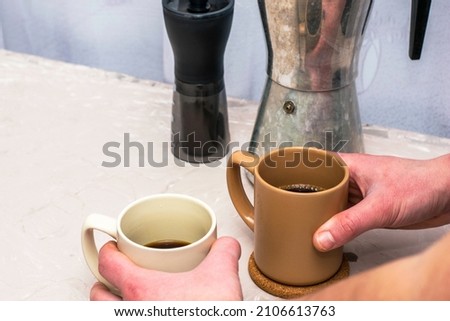 two mugs of coffee in the hands of a man next to a coffee grinder and a geyser on the table. High quality photo
