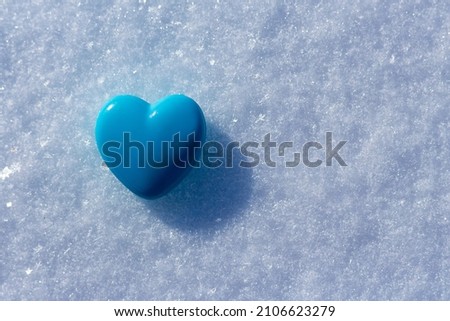 blue heart on pure white snow, photographed close-up and illuminated by bright sunlight, copy space