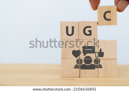 User-generated content concept.(UGC) Online marketing concept. Customer create content on social media . Close up hand put  wooden cube with "UGC"abbreviation and icon on white background,copy space Royalty-Free Stock Photo #2106636842