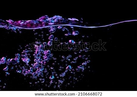 Clear water surface with ripple and bubbles in red and blue light on a black nature background