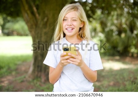 caucasian little kid girl wearing t-shirt standing outdoors taking a selfie  celebrating success