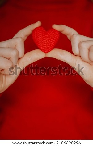 a person  in a red sweater holds a red knitted heart in his palms. valentine's day holiday symbol