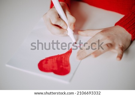 a person in a red sweater draws a card with a heart with a marker. valentine's day holiday symbol