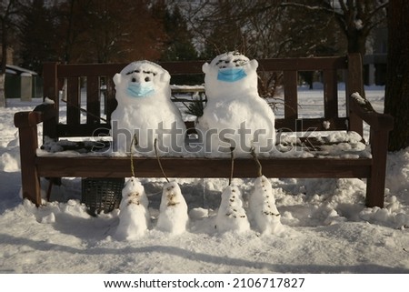 Two snowmen with mask sitting on bench in winter. Funny friends snowman in quarantine time.