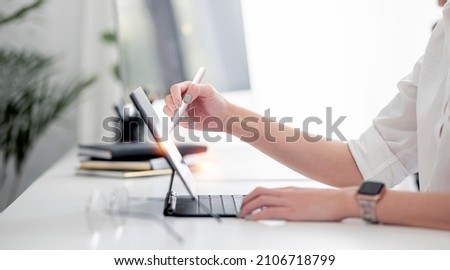 Woman using stylus pen on digital tablet while working from home office, cropped image.