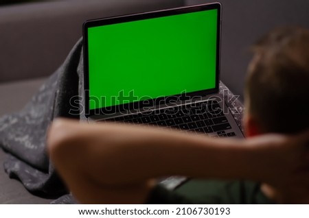 Caucasian man uses laptop with greenscreen of chromakey mockup. Person watches the video, relaxes, enjoys the rest on personal computer. Green screen and chroma key.
