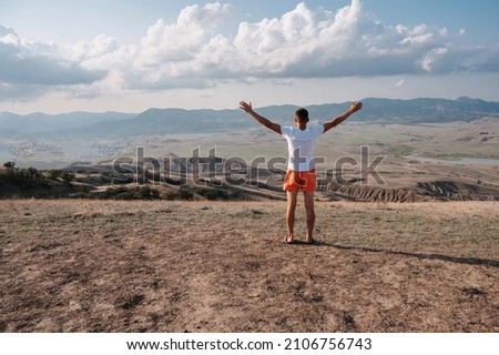 A young man stands with his hands up in the fresh air in a mountainous area. Place for your text