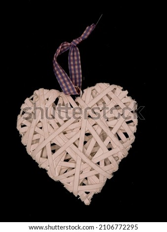 Heart shaped decoration made of wood, painted white with checkered ribbon. Wooden heart silhouette isolated, lying on black background. Decorative valentine heart as symbol of love, top view.