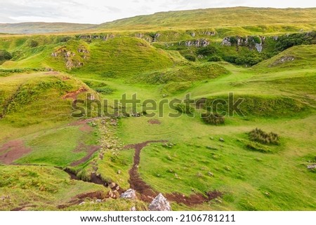 Landscape on the Isle of Skye in Scotland. Meadows of Fairy Glen with central circles on the green. Small hills with bushes and clouds in the sky. Well-trodden paths with earth in summer.