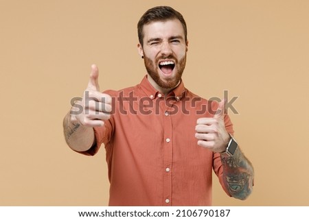 Laughing happy tatooed young brunet man 20s short haircut with earrings wears apricot shirt showing okay ok gesture wink isolated on pastel orange background studio portrait. People emotions concept,