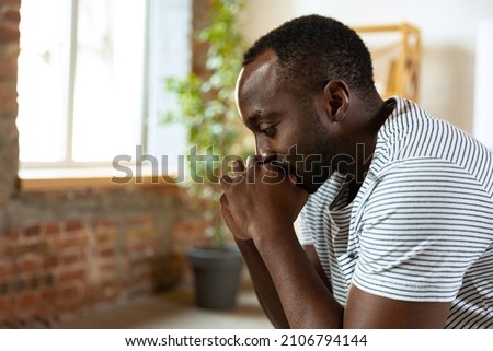 Portrait of young sad african man sitting and thinking about personal problems. Side view. Mental health, psychotherapy, depression, social issues, support, assistant concept. Looks despaired, unhappy Royalty-Free Stock Photo #2106794144