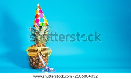 Pineapple in glasses and a festive hat with a pipe in his mouth on a blue background copy space. Fruit pineapple Creative holiday greetings