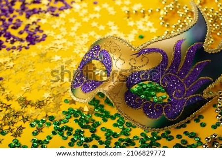 Mardi Gras gold color beads with Luxury Masquerade venetian festival carnival mask and golden, green, purple confetti on yellow background. Party invitation, greeting card,  carnivale celebration time