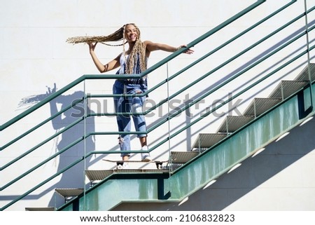 Black woman on an urban staircase, holding her coloured braids. Typical African hairstyle.