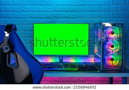 gaming chair and colorful bright rgb pc with keyboard mouse monitor with green screen copy space in front of LED light brick stone wall. Computer playing hardware games background