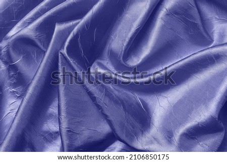 Blue violet color texture of draped shiny wrinkled silk. Background of folded satin cloth of trendy color of the year 2022 very peri. Elegant luxury crumpled fabric as design element. Top view.