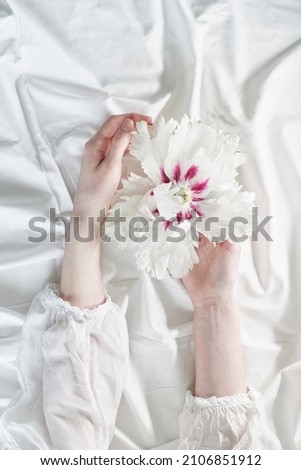 Creative floral greeting card. Beautiful spring aesthetics concept. Girls hands holding tender white-pink flower with white cloth background, top view with copy space. High quality photo