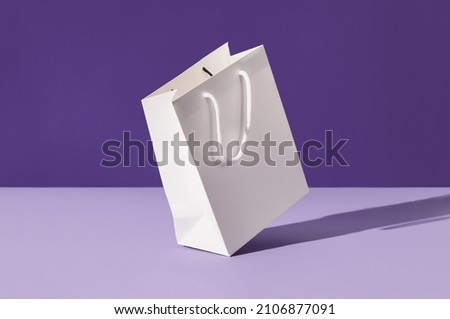 White floating paper shopping bag on purple background. Shopping sale delivery concept Royalty-Free Stock Photo #2106877091