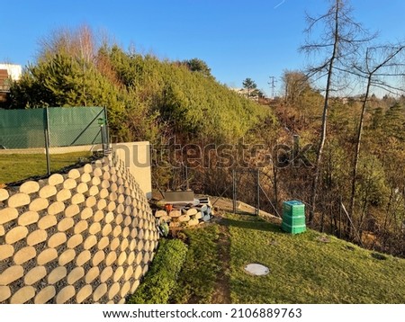 Support wall in the Czech Republic in Tabor town with wire fence on top of it. Concrete blocks make steep slope with stones inside. It separates different levels of the slope and creates gardens. Royalty-Free Stock Photo #2106889763