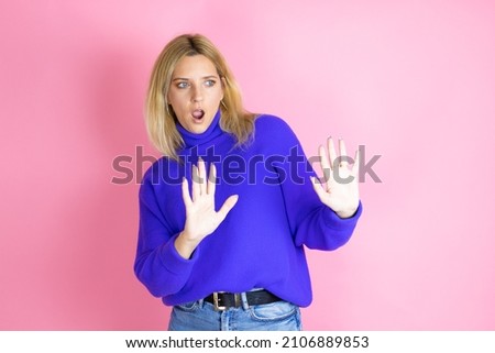 Young beautiful woman wearing casual sweater over isolated pink background afraid and terrified with fear expression stop gesture with hands, shouting in shock. Panic concept.