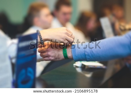Process of checking in on a conference congress forum event, registration desk table, visitors and attendees receiving a name badge and entrance wristband bracelet and register electronic ticket,  Royalty-Free Stock Photo #2106895178