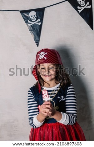 smiling little girl dressed as a pirate, looking at her number eight birthday candle