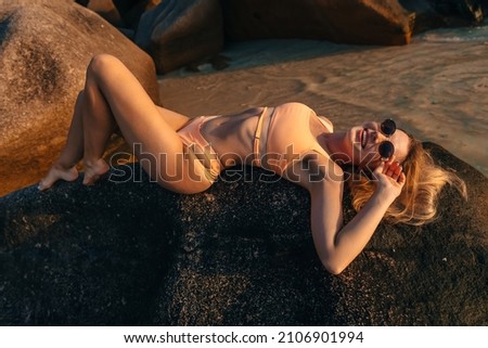 Young beautiful woman in swimsuit and lying on the stone. Summer holidays, vacation on a tropical island, sea and hot sand