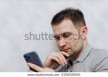 Handsome blogger guy in gray T-shirt holds an iPhone 12 Pro in his hand and communicates with subscribers