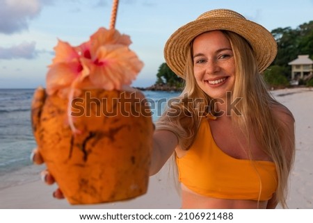 Portrait of attractive beautiful young woman in sunglasses drink cocktail from coconut shell through straw. Look straight on camera. Rest or vacation time. Trip to tropical country