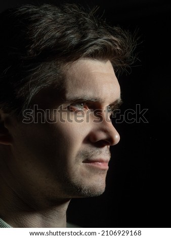 A thoughtful sad man looks to the right. portrait in side light, hard light, photo on black