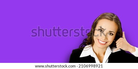 Businesswoman in black confident suit showing call me hand sign gesture, over purple violet background. Portrait of happy smiling gesturing brunette woman at studio. Business concept photo. Executive.