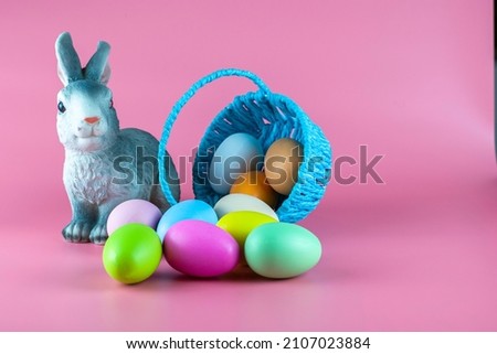 a rabbit and an inverted basket with easter eggs on a pink background copyscape. High quality photo