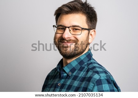 Portrait of one adult caucasian man 30 years old with beard and eyeglasses looking to the camera in front of white wall background smiling wearing casual shirt copy space Royalty-Free Stock Photo #2107035134