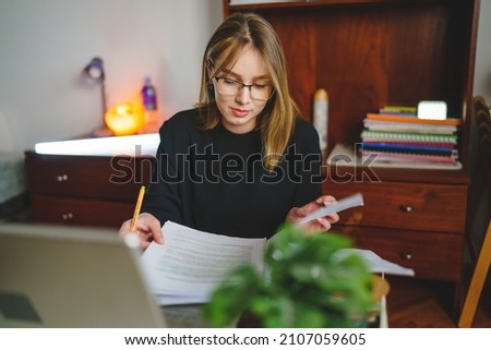 One young caucasian woman female student sitting at home writing and reading in her notebook holding pencil while study preparing for exam learning and education concept real people copy space Royalty-Free Stock Photo #2107059605