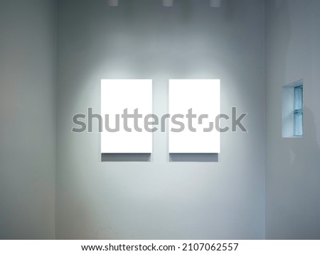 Two mockup vertical rectangle painting frames hanging on white wall background with spotlights. Blank white canvas frame with empty space in gallery, minimal style.